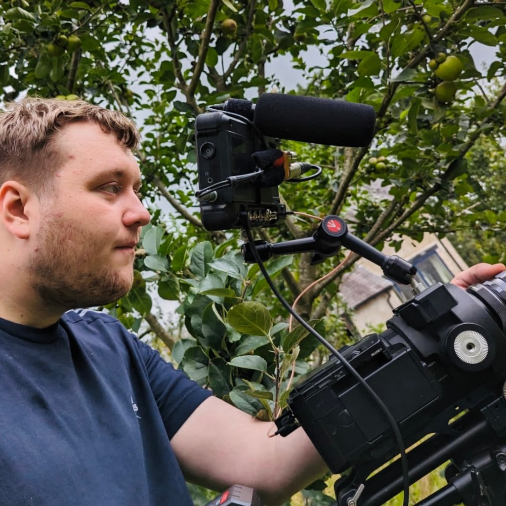 Person operating a professional camera in a garden setting, surrounded by greenery.